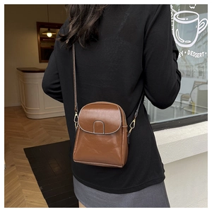 Brown vintage PU leather crossbody bag with white stitching shown on model in cafe