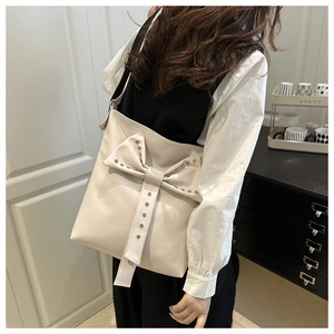 Close-up of cream tote bag with large studded bow detail and soft faux leather texture