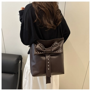 Detail of dark brown tote bag featuring a large leather bow and silver rivet accents