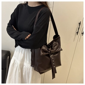 Detail of dark brown tote bag with large bow and silver studs on smooth PU leather surface