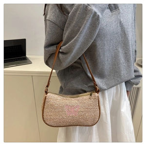 Dettaglio della borsa a spalla in paglia estiva con ricamo a farfalla rosa e finiture in pelle