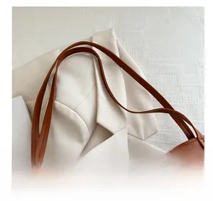 Detail of caramel brown leather tote bag straps against a white blazer background