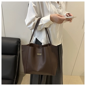 Close-up of a large dark brown faux leather tote bag with a small fashion logo label