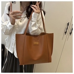 Detail of a large brown faux leather tote bag with FASHION lettering and slim shoulder straps