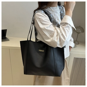 Detail of a black leather tote bag with FASHION label, worn on shoulder in office setting