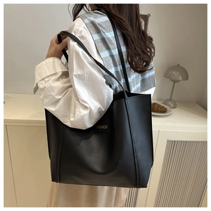 Detail of a black large capacity tote bag with fashion leather label on a model