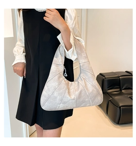 Detail einer halbmondförmigen Hobo-Tasche mit Faltenstruktur und metallischem Finish