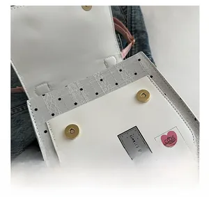 Close-up of white flap bag with gray polka dot mesh, magnetic buckles and cute patches
