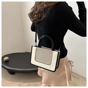 Detail of a contrast canvas and leather tote bag styled by a model in a minimal setting