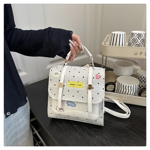Detailed view of white polka dot handbag featuring gold hardware and a top handle