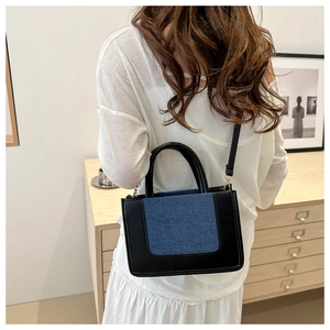 Detail of contrast patchwork handbag featuring black leather and blue denim material