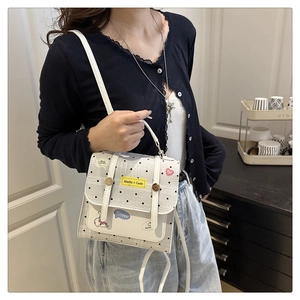 Detail of a white polka dot crossbody bag featuring colorful cartoon patches on PU leather
