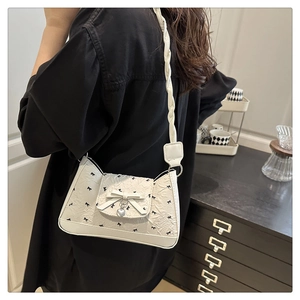 Detail of cream underarm bag with black bow patterns and silver heart pendant