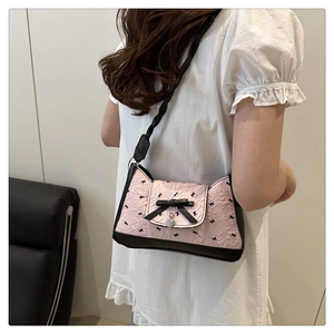 Détail du sac à bandoulière rose froncé avec nœuds noirs et breloque en forme de cœur