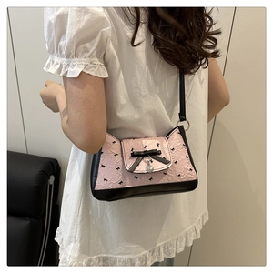 Detail of pink pleated fabric with black bow accent and silver heart charm on handbag