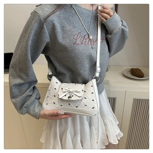 Vue détaillée du sac bandoulière blanc avec nœuds noirs et pendentif en forme de cœur