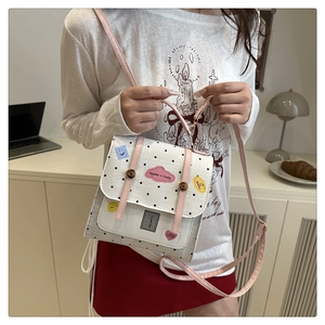 Detailed view of white polka dot square bag with pink straps and cartoon patches