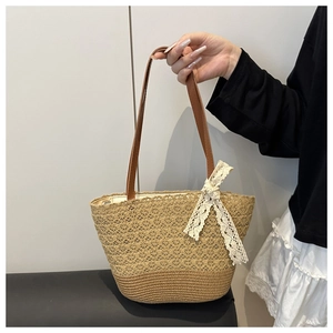 Detail of woven straw tote bag featuring white lace bow and brown leather shoulder strap