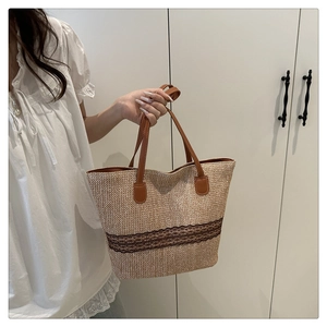 Side view of a straw tote bag with brown lace embroidery and leather straps on a model