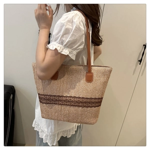 Detail of woven straw tote bag with brown lace trim and faux leather handle shown on shoulder