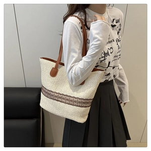 Detail of woven straw tote bag with brown leather handles and lace embroidery detail