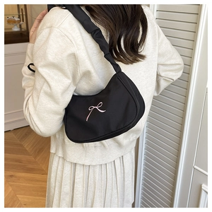 Close-up of black nylon hobo bag with pink bow embroidery and ruffled strap on shoulder
