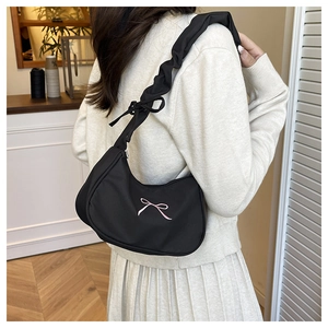 Detail of black hobo bag with pink bow embroidery and pleated strap on model shoulder