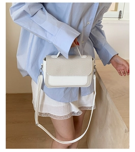 Detail of cream crossbody bag with textured woven flap and silver metal buckle closure
