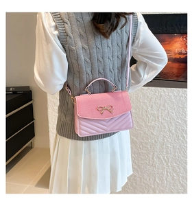 Pink crossbody bag with gold bow clasp shown on model in a modern indoor setting