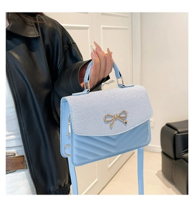 Detail of light blue crossbody bag with golden bow hardware and V-quilted texture