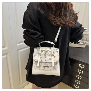 Close-up of white floral handbag with bow and heart charm on a model for scale
