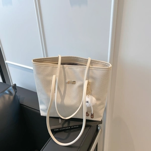 Sac cabas beige tressé avec fines anses et charm en peluche sur un canapé chic