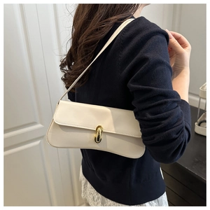 Primo piano di una borsa baguette beige con fibbia dorata sulla spalla della modella