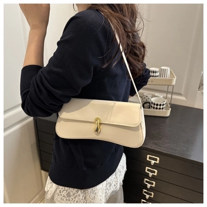 Detail view of a beige leather shoulder bag with gold clasp shown on a model side profile