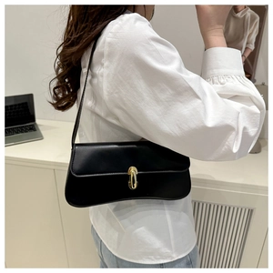 Vista laterale di una borsa sottobraccio nera lucida con fibbia dorata indossata dal modello