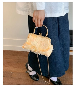 Detail view of cream floral evening shell bag with golden metal handle and chain strap