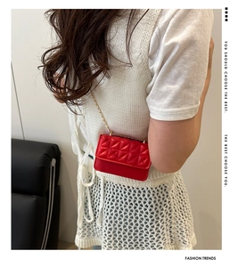Detail of red quilted crossbody bag with gold chain strap on a white knit outfit