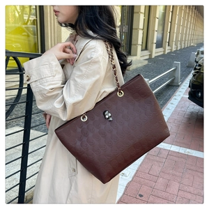 Detail of a brown tote bag with skull embossing and a metal skull buckle on a beige coat