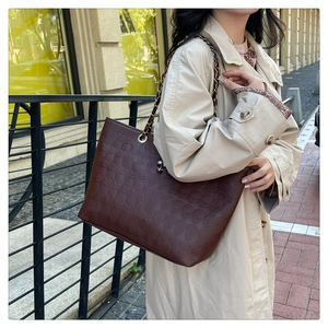 Detail of dark brown tote bag with skull embossed texture and chain shoulder strap
