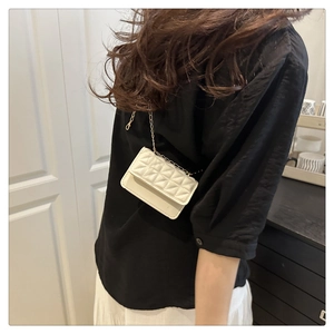 Close-up of white quilted mini bag with elegant gold chain strap worn by a model