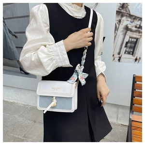 Detailed close-up of a blue and white square crossbody bag with floral scarf and charm