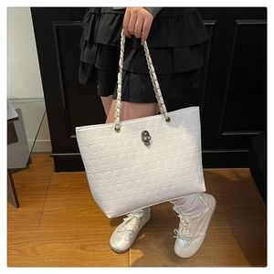 Détail d'un sac cabas blanc avec motifs tête de mort gaufrés et poignée en chaîne dorée