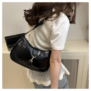 Close-up of black glossy leather underarm bag with gold buckle on a model