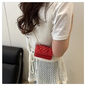 Detail view of mini red quilted crossbody bag with gold chain strap worn by model