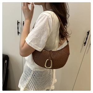 Detail of a brown croc-embossed half-moon shoulder bag with a gold buckle and knot strap