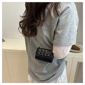 Detail of a quilted black mini crossbody bag with a gold chain strap on a model