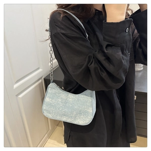 Détail d'un sac à bandoulière bleu clair texturé avec chaîne argentée sur un modèle