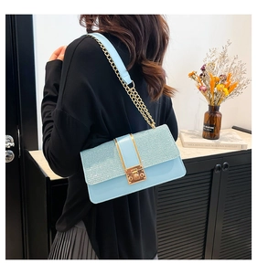Detail of light blue crossbody bag with glitter flap and golden chain strap on a model