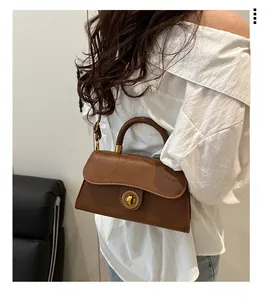 Detail of vintage brown leather satchel with round metal twist lock on a white shirt