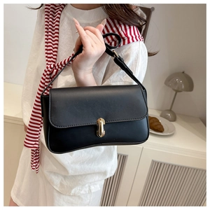 Detail of black leather underarm bag with gold metal clasp held by a model in a stylish room